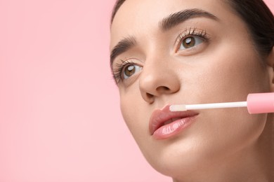Photo of Woman applying lip gloss on pink background, space for text