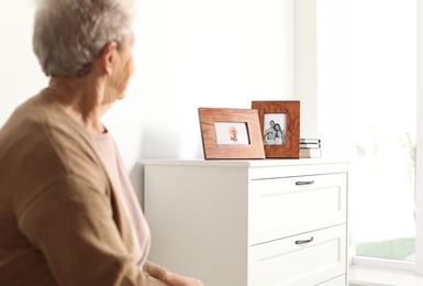 Photo of Elderly woman looking at framed family portraits indoors