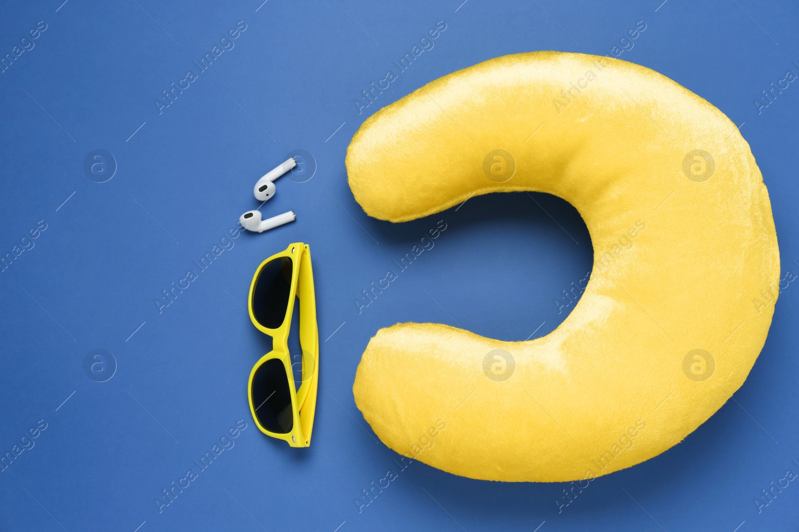 Photo of Yellow travel pillow, sunglasses and earphones on blue background, flat lay. Space for text