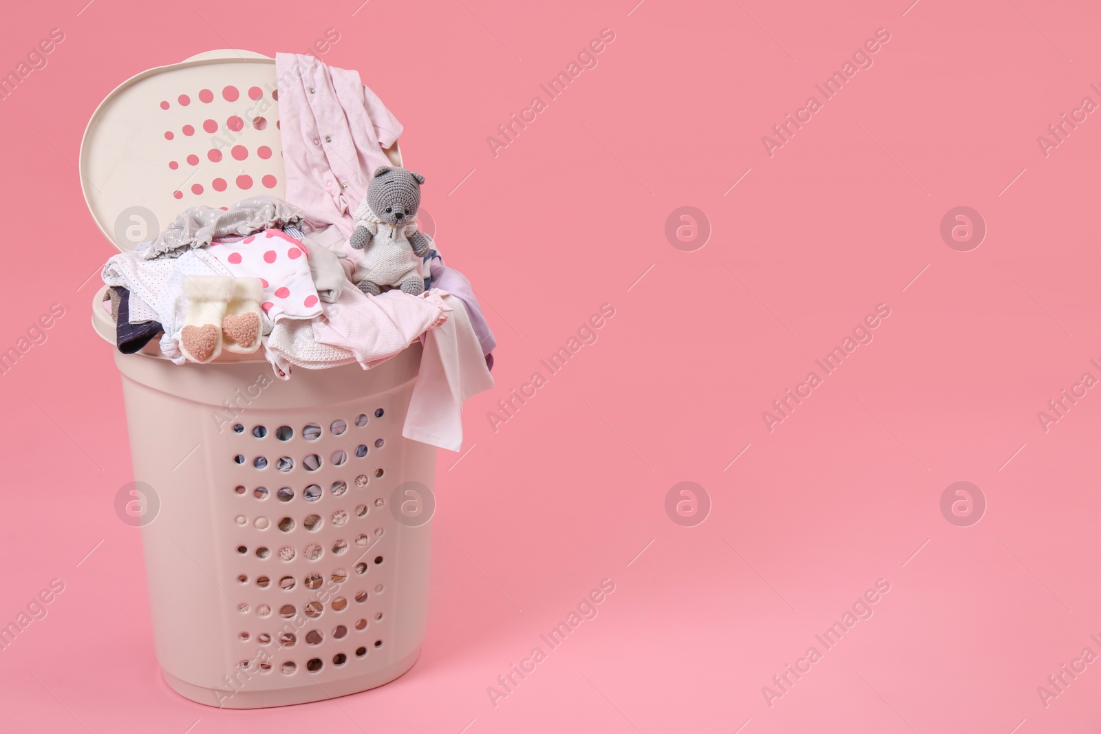 Photo of Laundry basket with baby clothes and soft toy on light pink background. Space for text