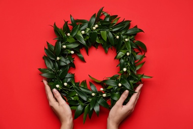 Photo of Woman with beautiful mistletoe wreath on red background, top view. Traditional Christmas decor