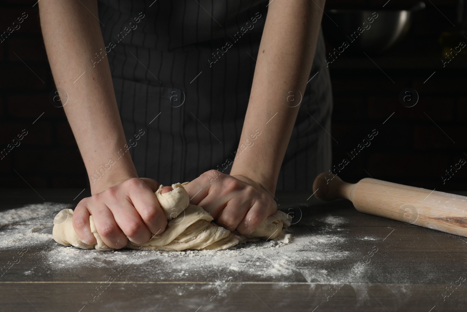 Photo of Making bread. Woman kneading dough at wooden table in kitchen, closeup