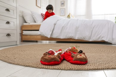 Photo of Cute little boy in bed at home, focus on slippers with treats. Saint Nicholas day tradition