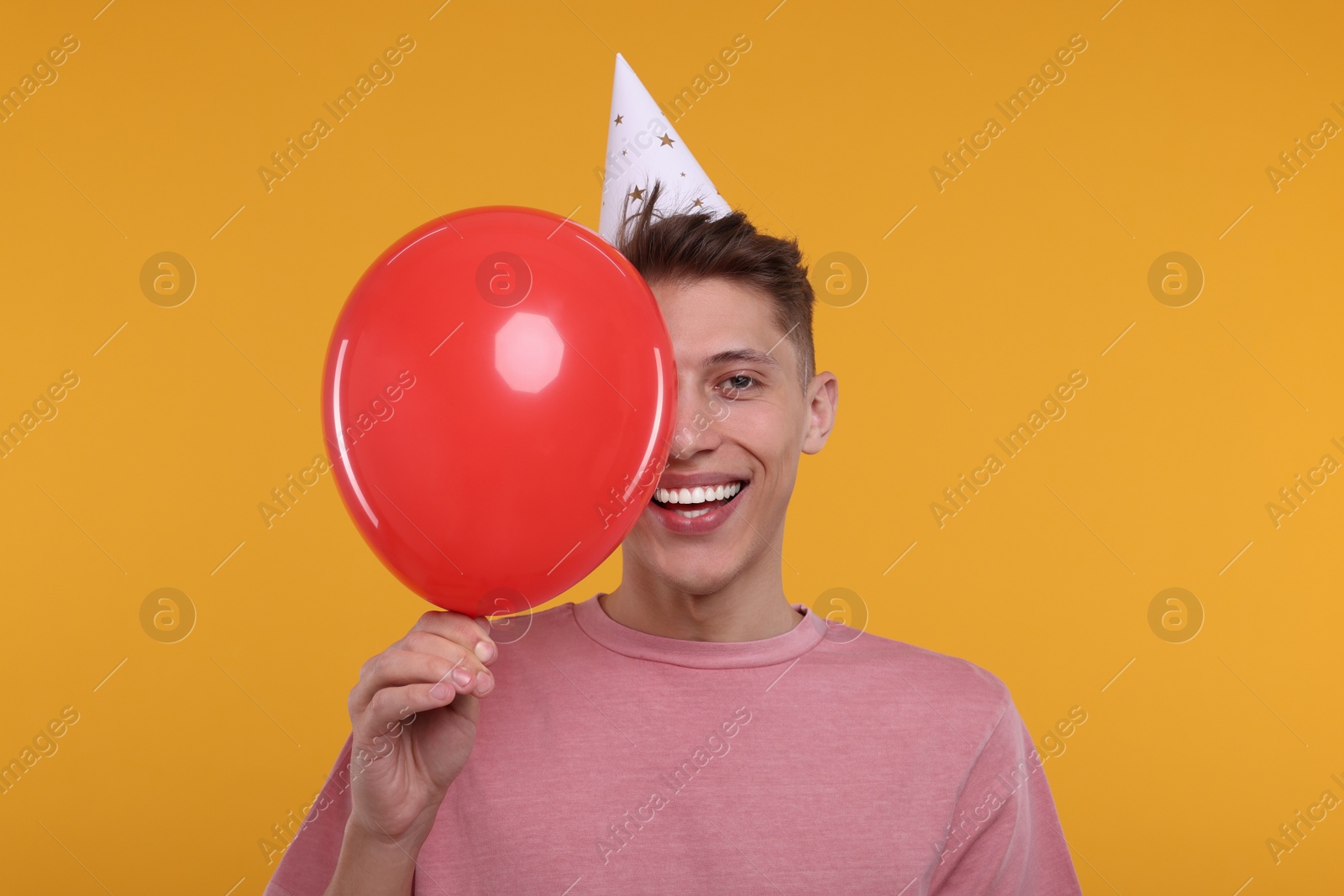 Photo of Happy man in party hat with balloon on orange background