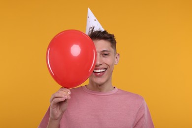 Photo of Happy man in party hat with balloon on orange background