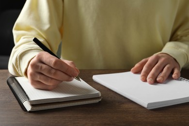 Woman with pen and notepads at wooden table, closeup