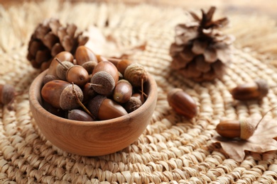 Photo of Acorns in wooden bowl on wicker mat. Space for text