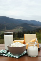 Photo of Tasty cottage cheese and other fresh dairy products on wooden table in mountains