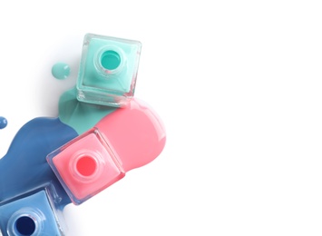 Photo of Spilled different nail polishes with bottles on white background, top view