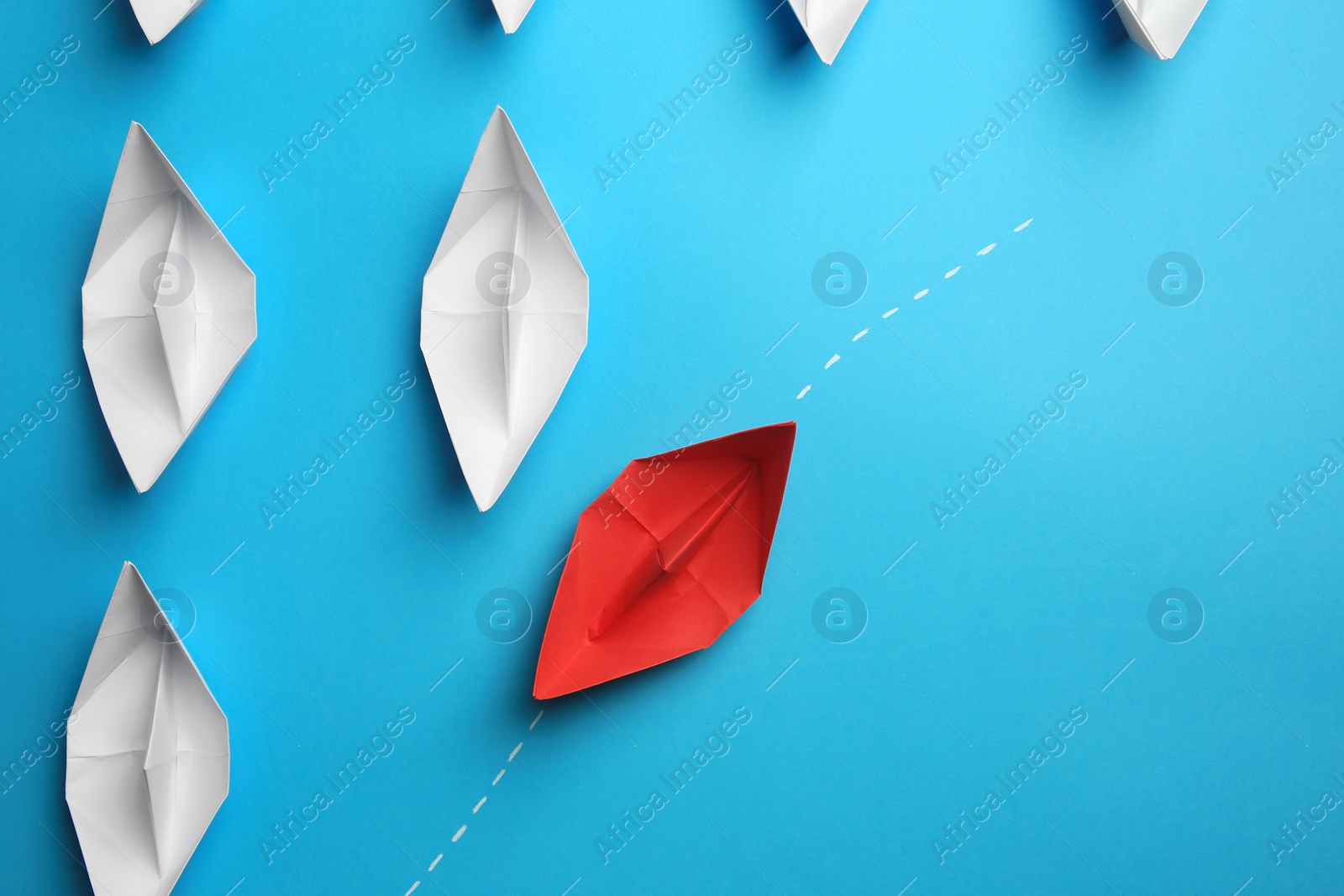 Photo of Red paper boat floating to others on light blue background, flat lay with space for text. Uniqueness concept