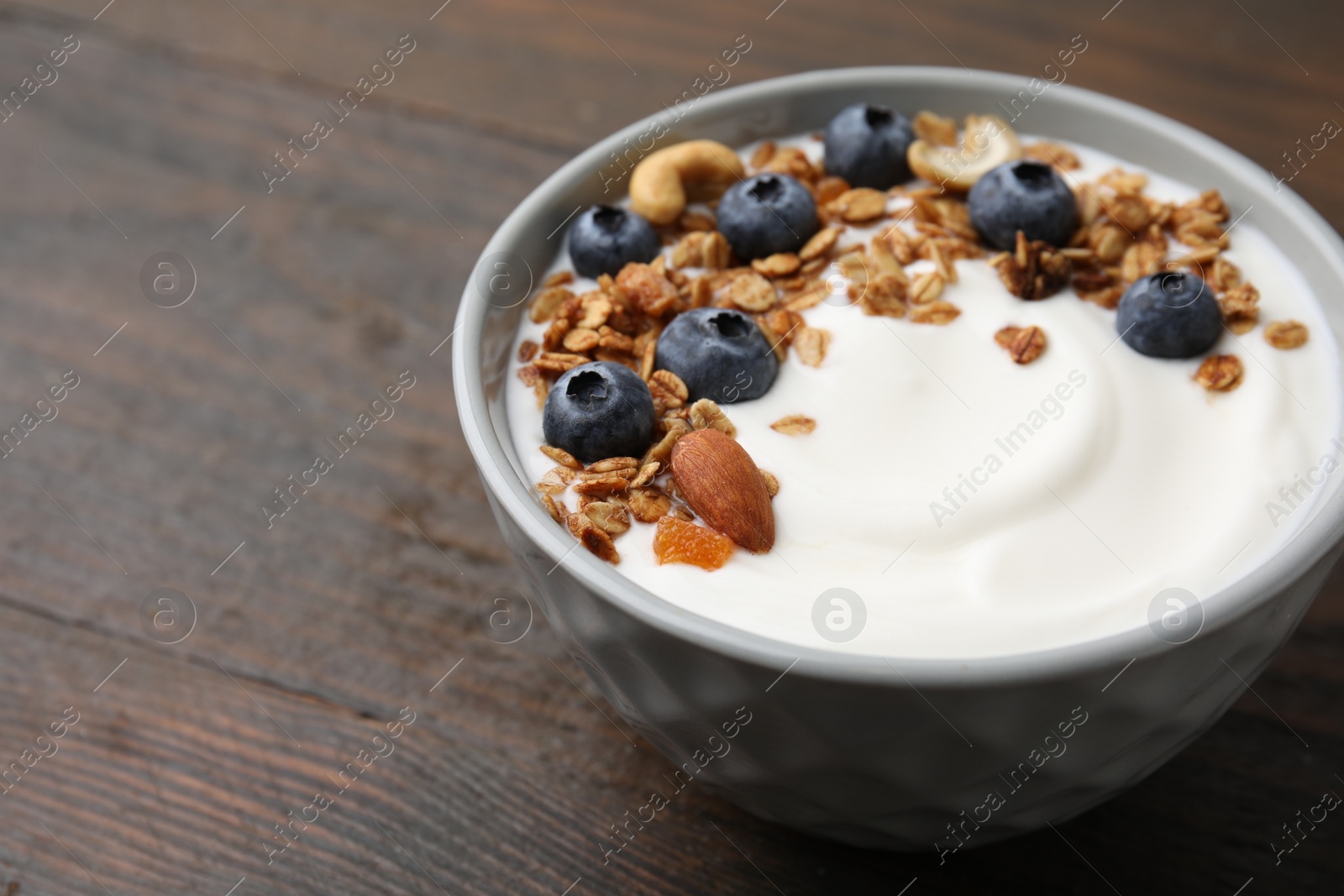 Photo of Bowl with yogurt, blueberries and granola on wooden table, closeup. Space for text