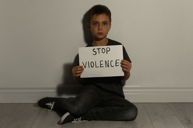 Photo of Abused little boy with sign STOP VIOLENCE near white wall. Domestic violence concept