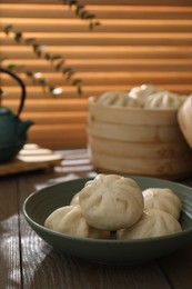 Photo of Delicious bao buns (baozi) in bowl on wooden table, closeup