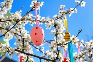 Photo of Beautifully painted Easter eggs hanging on blooming cherry tree outdoors