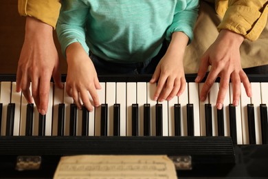 Photo of Young woman with child playing piano, top view. Music lesson