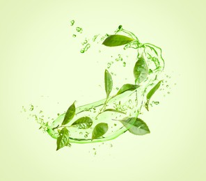 Image of Splashes of refreshing drink with leaves on pale green background. Green or matcha tea