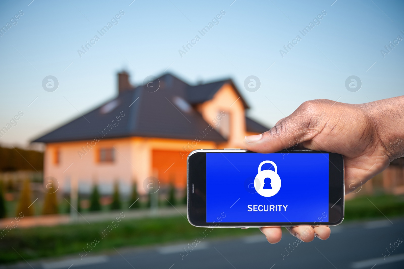 Image of Home security system. African American man with smartphone near his house outdoors, closeup