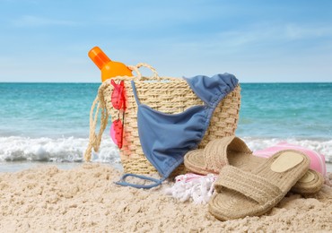 Image of Stylish bag with different accessories on sandy beach near ocean