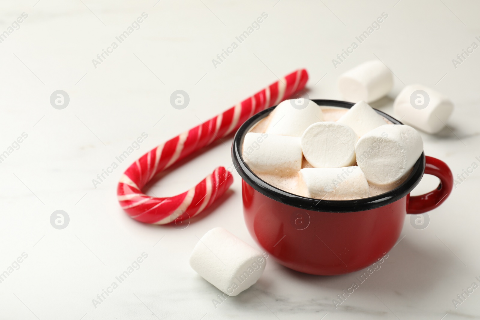 Photo of Tasty hot chocolate with marshmallows and candy cane on white marble table, closeup. Space for text