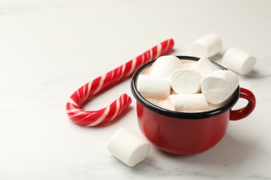 Tasty hot chocolate with marshmallows and candy cane on white marble table, closeup. Space for text