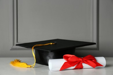 Graduation hat and diploma on white table near grey wall