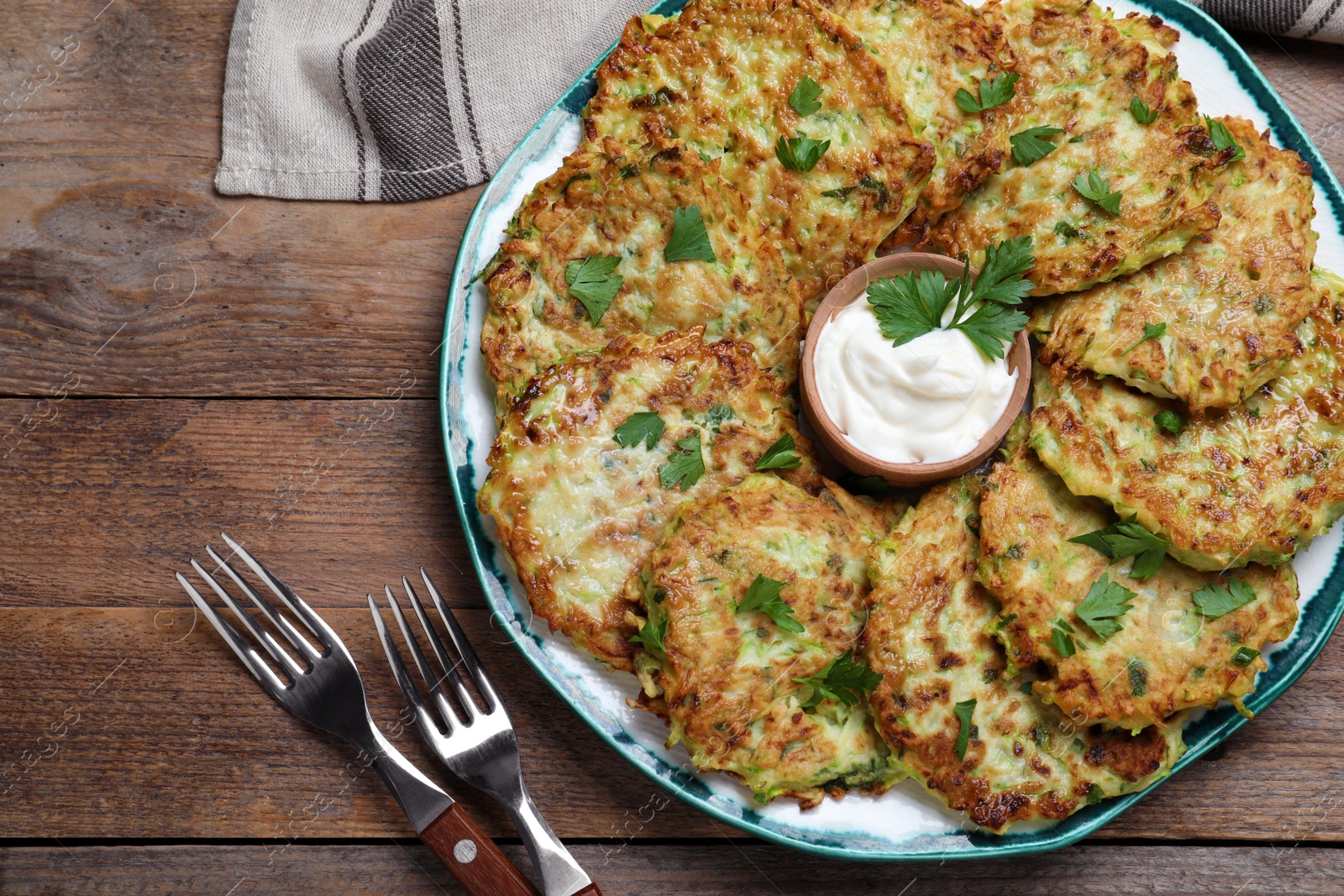 Photo of Delicious zucchini fritters with sour cream served  on wooden table, flat lay