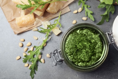 Jar of tasty arugula pesto and ingredients on grey table, flat lay