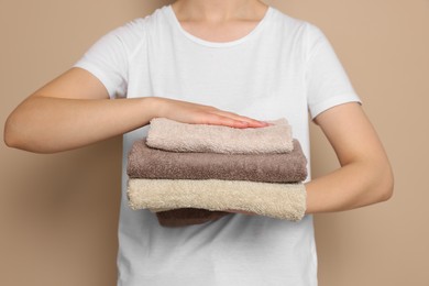 Photo of Woman holding folded soft terry towels on light brown background, closeup