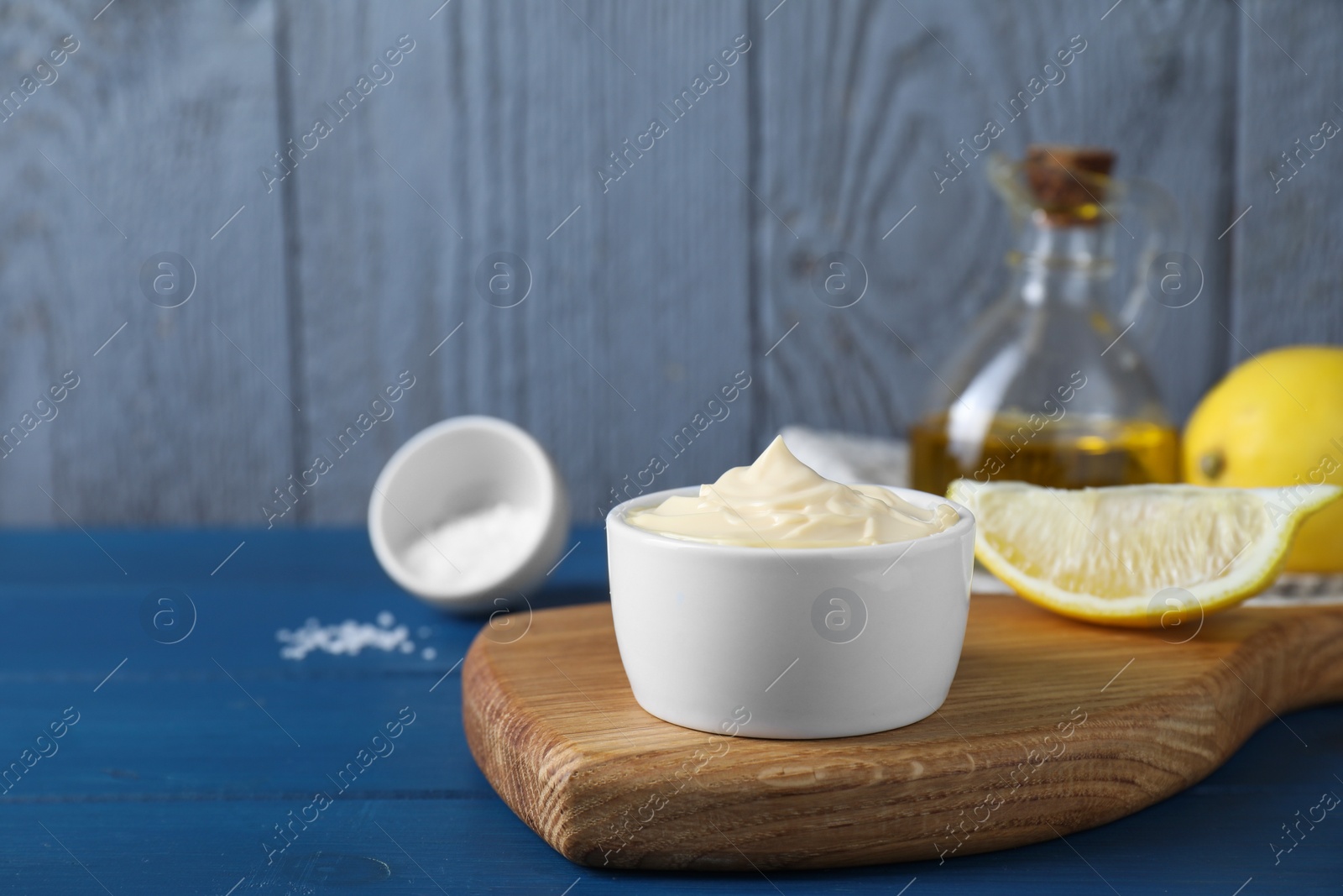 Photo of Tasty mayonnaise in bowl and lemon wedge on blue wooden table, space for text