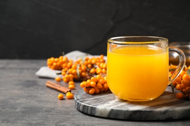 Photo of Delicious sea buckthorn tea and fresh berries on grey table. Space for text