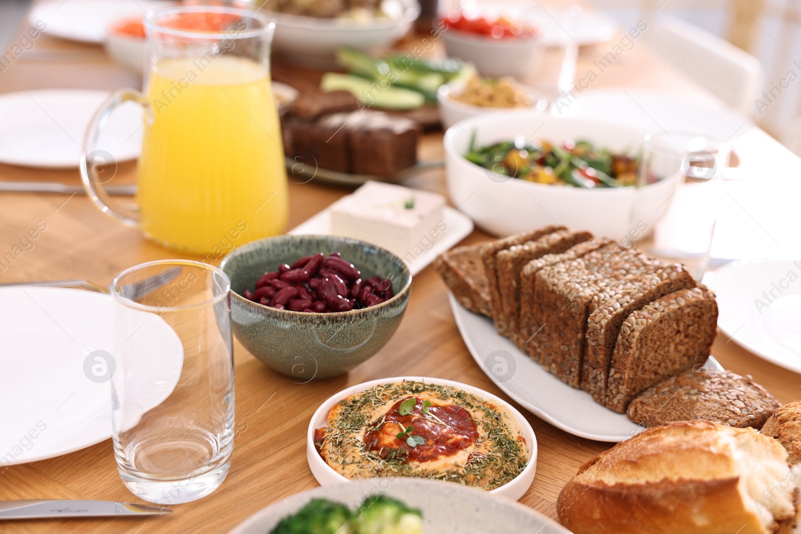 Photo of Healthy vegetarian food, jug of juice, glasses, cutlery and plates on wooden table indoors