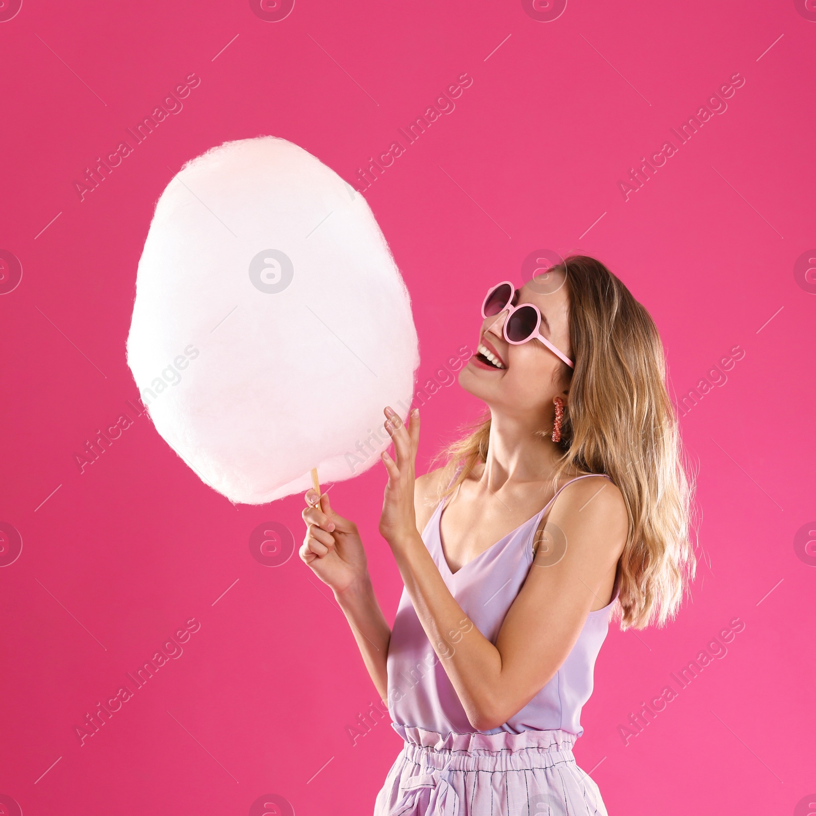 Photo of Happy young woman with cotton candy on pink background