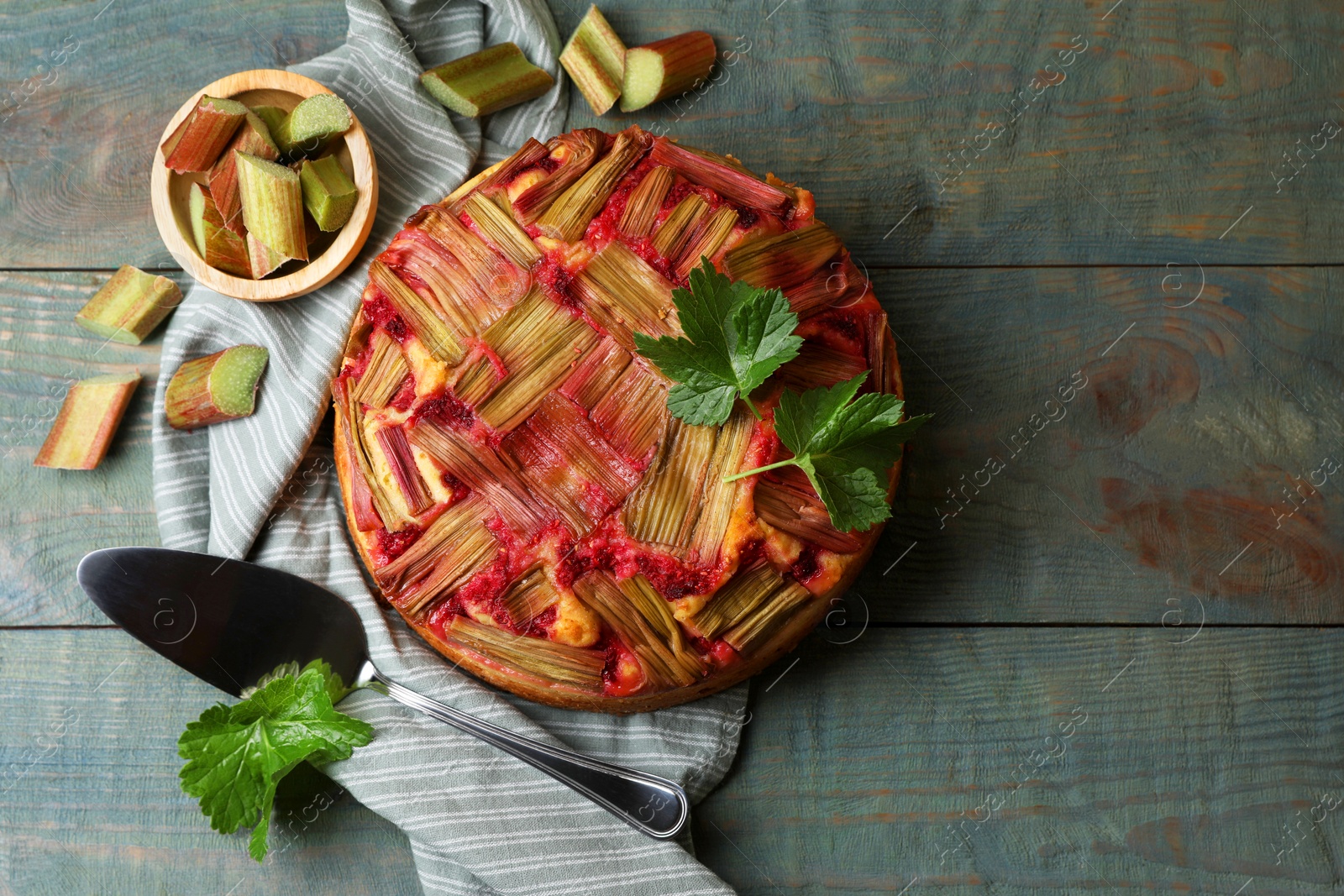 Photo of Freshly baked rhubarb pie, cut stalks and cake server on wooden table, flat lay. Space for text