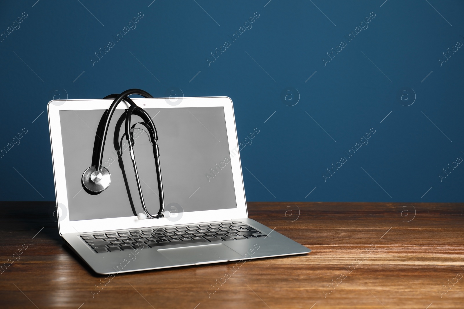 Photo of Modern laptop with stethoscope on table against color wall. Mockup for design