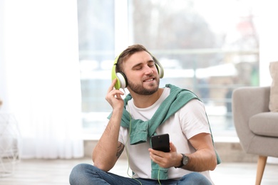 Photo of Young man with headphones and mobile device enjoying music in living room