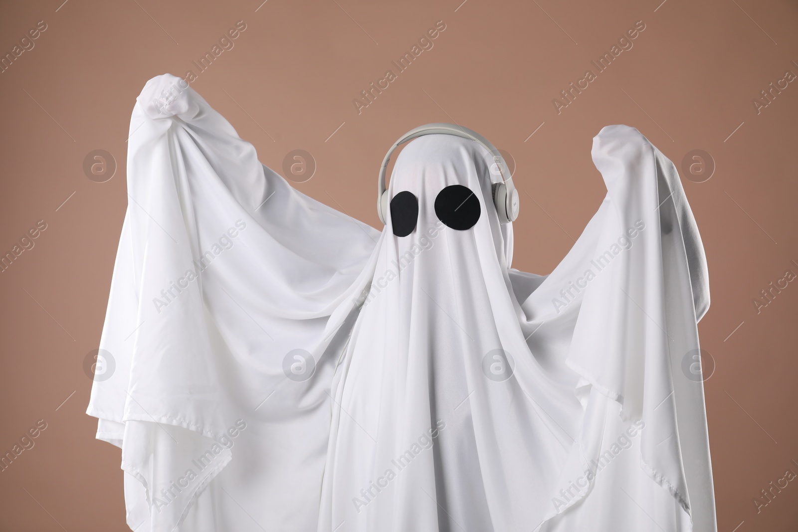 Photo of Person in ghost costume wearing headphones on dark beige background