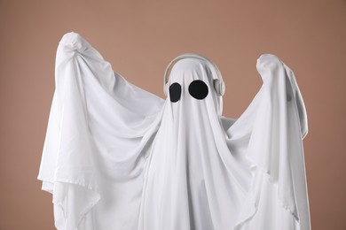 Photo of Person in ghost costume wearing headphones on dark beige background