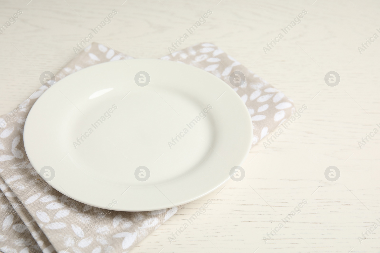 Photo of Empty plate and napkin on white wooden table, closeup