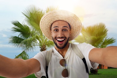 Image of Smiling young man in straw hat taking selfie at resort