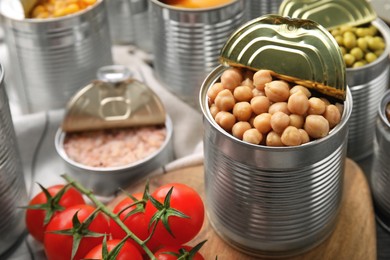 Photo of Open tin cans with chickpeas and different products on wooden table, closeup