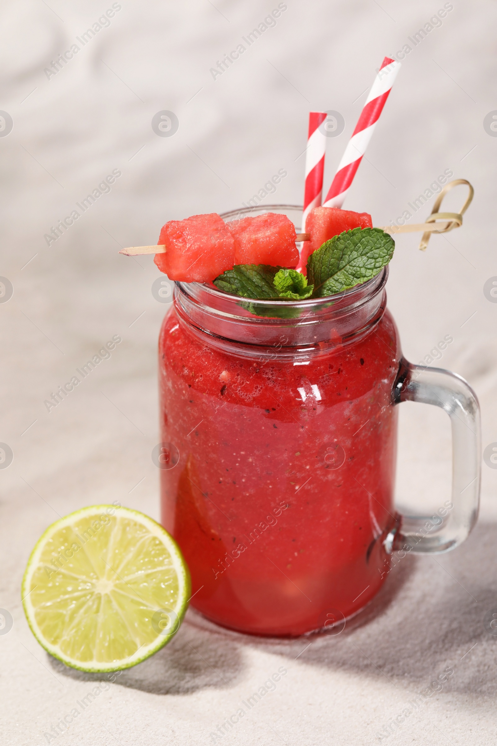 Photo of Tasty watermelon drink with lime in mason jar on sand