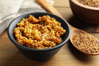 Photo of Whole grain mustard in bowl and dry seeds on wooden table, closeup