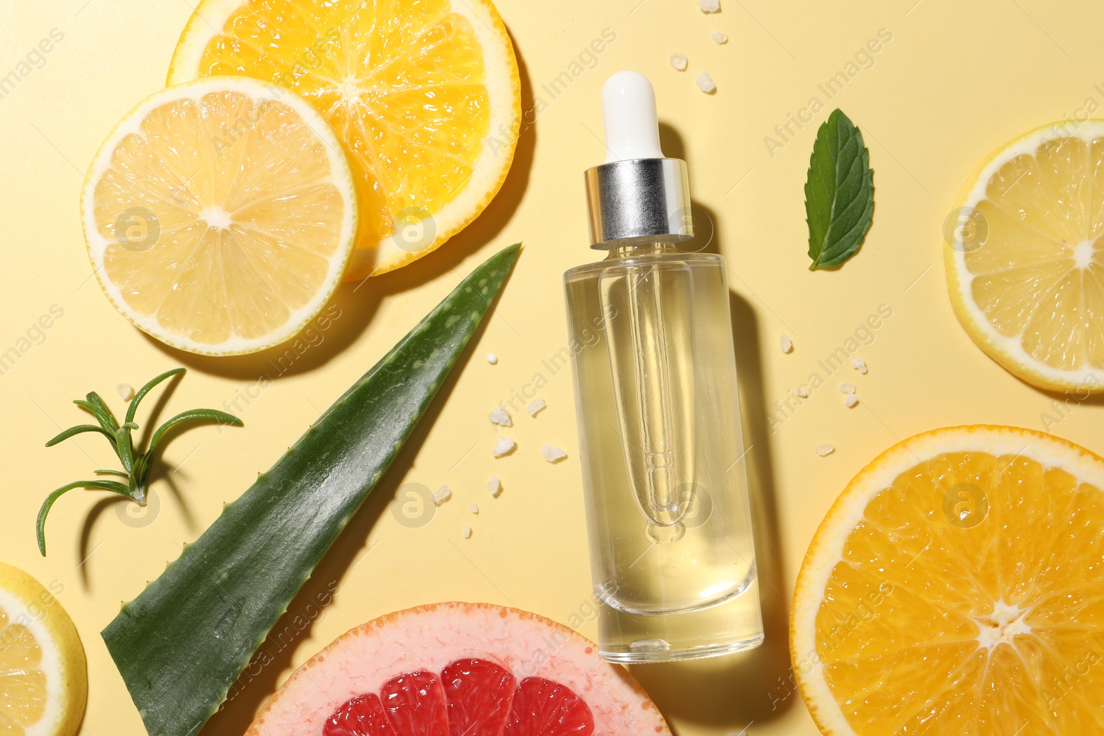 Photo of Bottle of cosmetic serum, sliced citrus fruits and aloe vera leaf on yellow background, flat lay