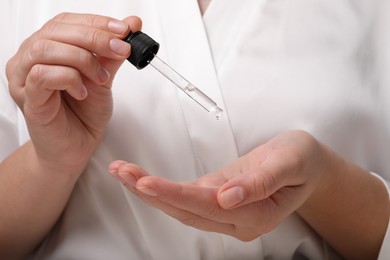 Photo of Woman applying cosmetic serum onto hand, closeup