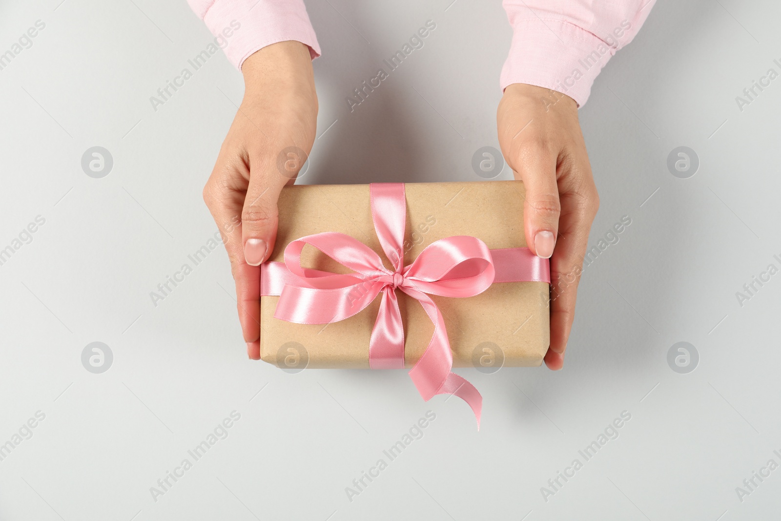 Photo of Woman holding gift box on light background, top view