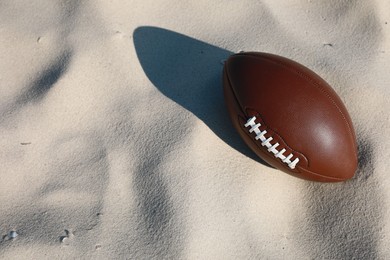 Photo of American football ball on sand, above view. Space for text
