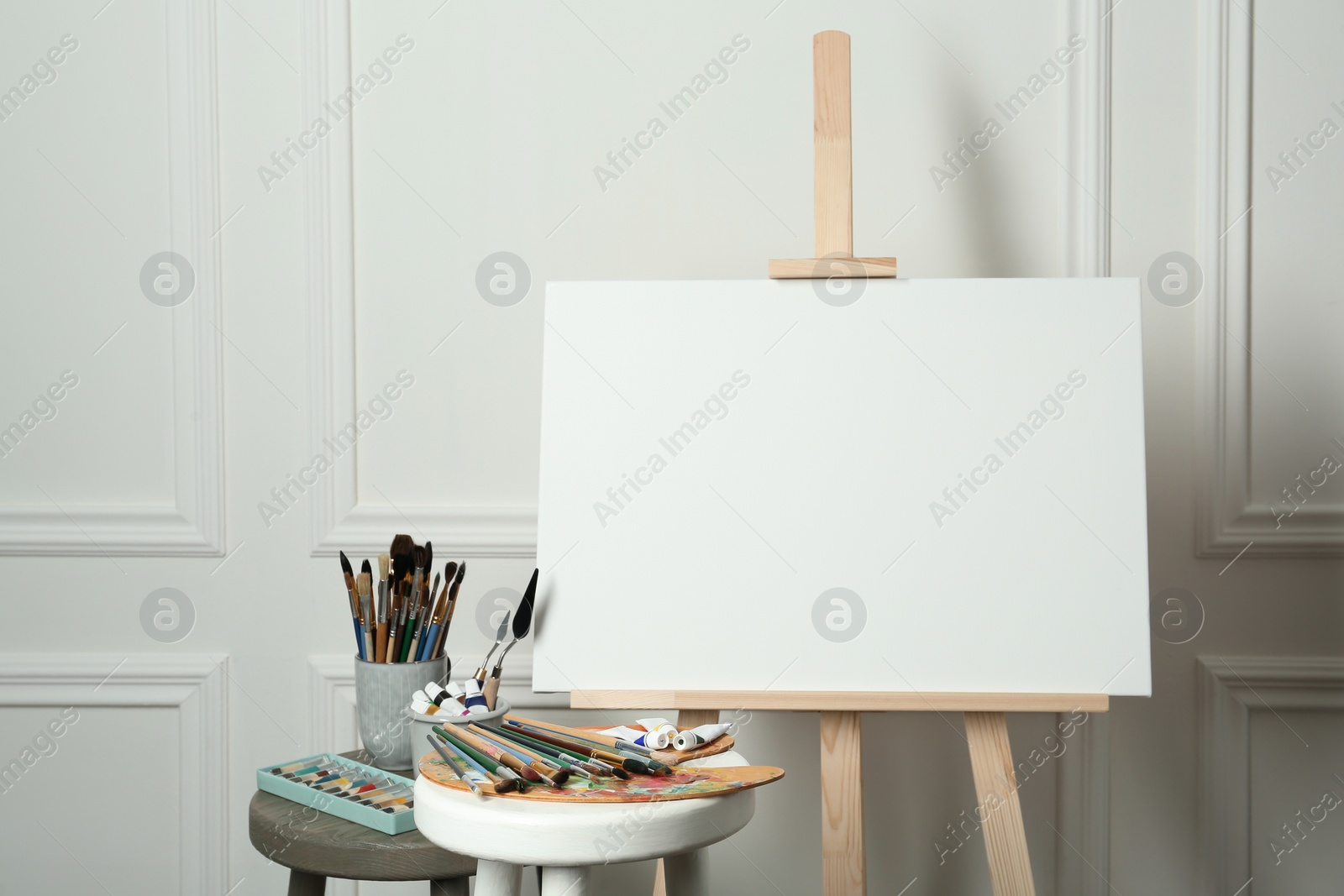 Photo of Easel with blank canvas, brushes, paints and palette in studio