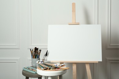 Easel with blank canvas, brushes, paints and palette in studio