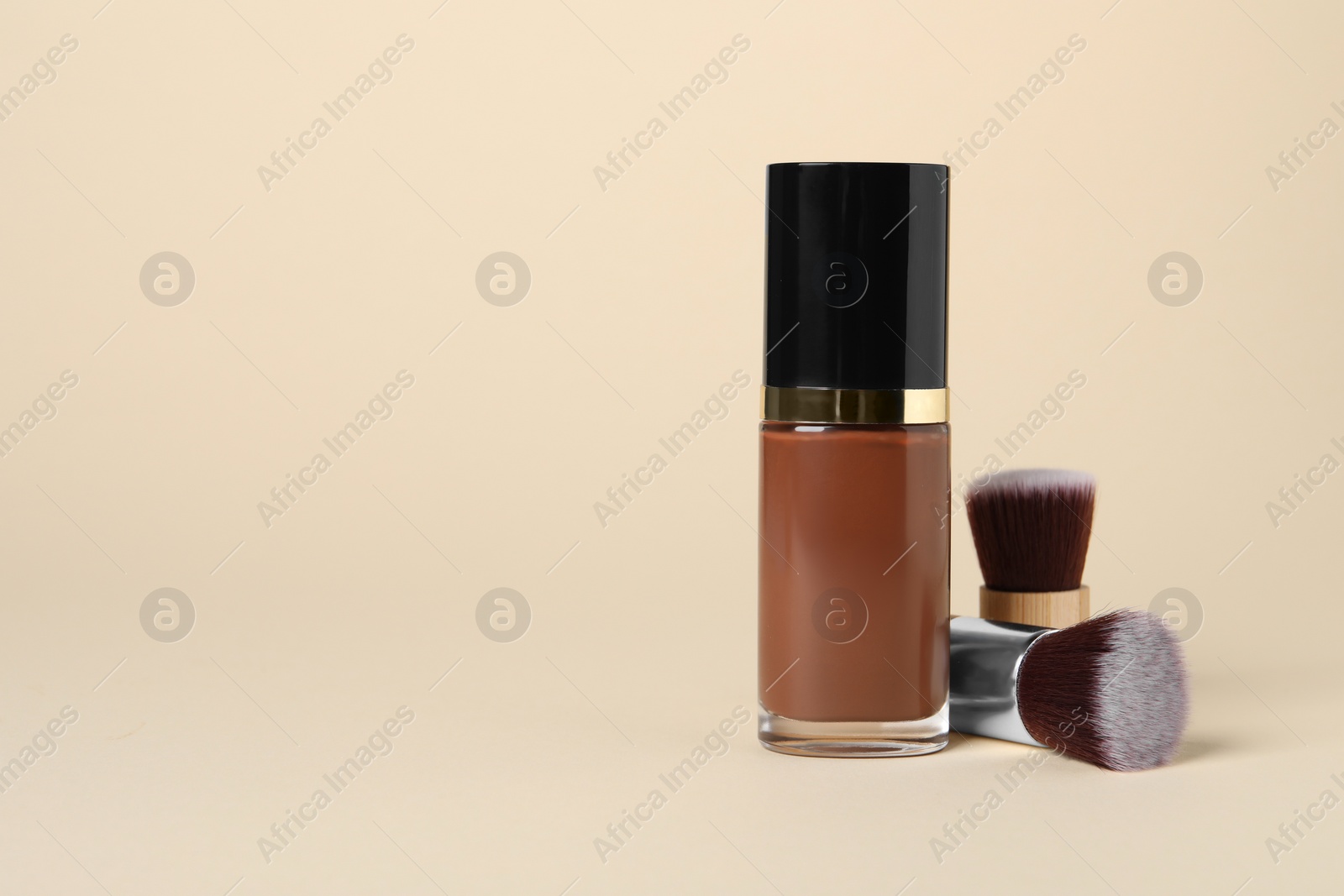 Photo of Bottle of skin foundation and brushes on beige background, space for text. Makeup product