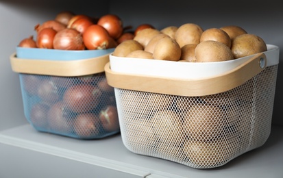 Photo of Baskets with potatoes and onions on shelf. Orderly storage